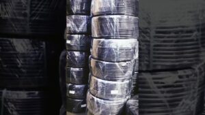 Rollos negros de tubería apilados y envueltos en film transparente en un almacén, fotografía descriptiva que apoya la consulta Tuberías de polietileno ventajas y desventajas para tu proyecto al mostrar estado, embalaje y facilidad de manejo.