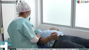 Profesional de salud con gorro, bata y cubrebocas atiende y sostiene el brazo de un paciente recostado en una camilla dentro de un consultorio luminoso, en una escena que sugiere orientación sobre opciones y procedimiento, ilustrando información sobre Vasectomía sin bisturí ventajas y desventajas clave para decidir