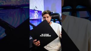 Imagen vertical de un creador joven con camiseta blanca sentado en una silla gaming frente a dos monitores con fondos morado y azul, micrófono y luces RGB, sosteniendo un panel negro con texto visible y el título Ventajas y desventajas fuentes de energía: qué opción elegir para describir de forma accesible y optimizada el contenido.