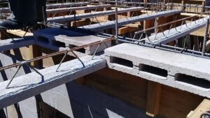 Imagen de una losa en construcción con viguetas prefabricadas de hormigón y bovedillas huecas apoyadas sobre encofrado de madera y armadura de acero, Losa de vigueta y bovedilla ventajas y desventajas clave para describir visualmente su montaje, ligereza relativa, continuidad estructural y la necesidad de refuerzo y encofrado temporal.