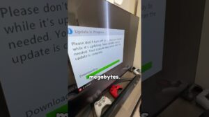 Televisor mostrando un mensaje de actualización en curso con barra de progreso y texto en inglés, varios mandos de Xbox 360 y una barra sensora sobre un mueble, Rgh Xbox 360 ventajas y desventajas para modificar tu consola, descripción optimizada para SEO y accesibilidad que resalta el proceso de descarga, la presencia de controles y la posibilidad de reinicio durante la instalación.