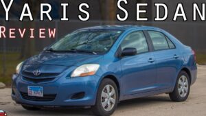 Sedán compacto Toyota Yaris azul estacionado en exterior, vista frontal lateral derecha que muestra faros, espejos negros, llantas con tapacubos y carrocería de cuatro puertas, ideal para ilustrar reseñas y comparativas, Ventajas y desventajas Toyota Yaris 2007: ¿vale la pena?
