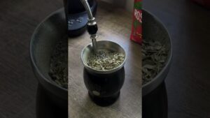 Primer plano de un mate negro con borde metálico y bombilla insertada entre hojas secas de yerba mate, con un paquete en segundo plano, imagen optimizada para accesibilidad y SEO que ilustra Ventajas y desventajas de la yerba mate: secretos y riesgos reales