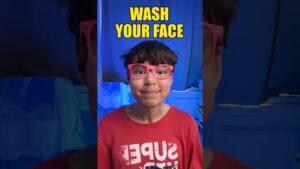 Niño sonriente con gafas rosas y camiseta roja frente a un fondo iluminado en azul y con el texto amarillo en la parte superior que dice "WASH YOUR FACE", Ventajas y desventajas de YouTube para niños: guía para padres.