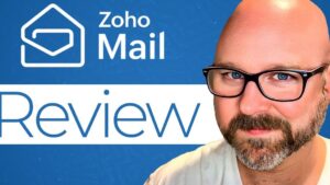 Miniatura con fondo azul que muestra el logotipo y el texto Zoho Mail junto a la palabra Review a la izquierda y un primer plano de un hombre calvo con gafas y barba a la derecha, destinada a ilustrar Ventajas y desventajas de Zoho Mail: ¿es el correo ideal para ti?
