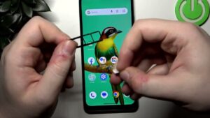 Manos que sostienen la bandeja SIM y una tarjeta nanoSIM frente a un smartphone con fondo de pantalla de un pájaro, imagen útil para guías de insertar SIM y reseñas del dispositivo ZTE Blade V50 ventajas y desventajas para decidir si vale la pena